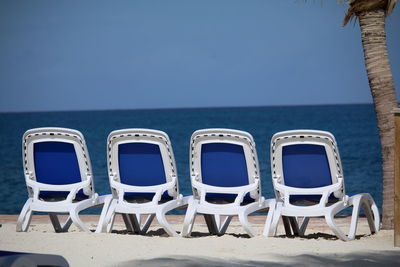 Deck chairs on beach against clear blue sky