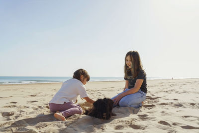 Rear view of two girl sitting at beach against clear sky