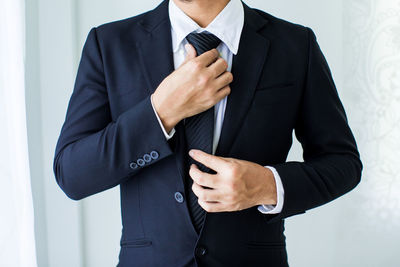 Midsection of businessman adjusting tie
