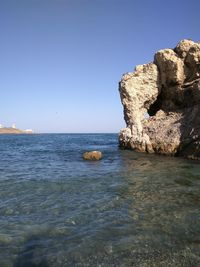 Rock formations in sea against clear blue sky