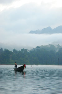 Man on longtail boat in lake against cloudy sky