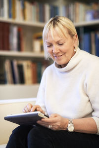 Mid adult woman using mobile phone while sitting on book