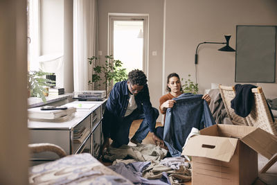 Couple helping each other while sorting out old clothes at home