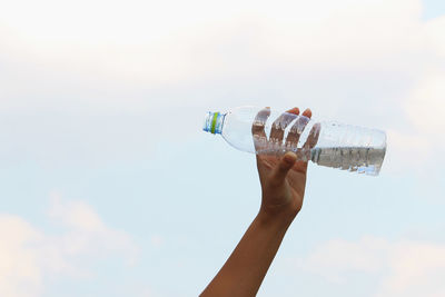 Low angle view of hand holding glass bottle against sky
