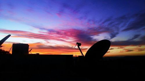 Silhouette of buildings and satellite dish against dramatic sky during sunset