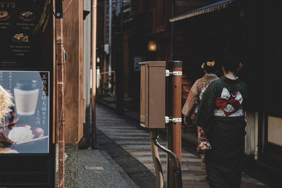 Rear view of people standing on footpath by building