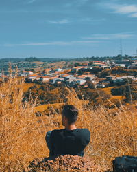 Rear view of man sitting on field against sky