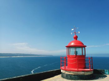 Red lighthouse by sea against blue sky