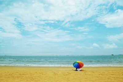 Rear view of woman under umbrella sitting at beach