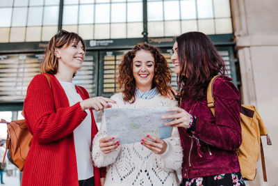 Cheerful women holding map while standing outdoors