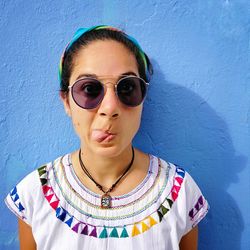 Portrait of woman wearing sunglasses while sticking out tongue against wall