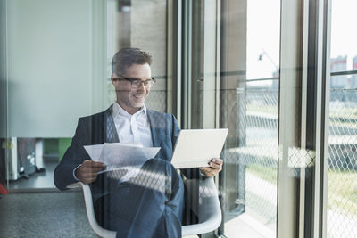 Smiling businessman with documents looking at tablet
