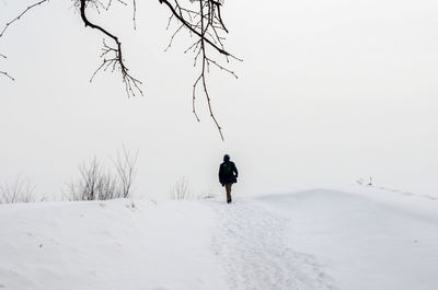 Man walking on snow covered landscape against sky