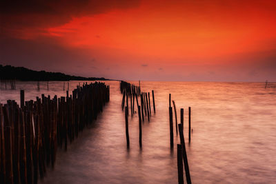 Wooden posts in sea against orange sky