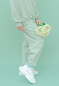 Low section of woman holding flowering bouquet standing over colored background