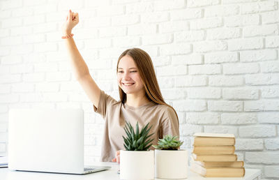 Young woman using phone while standing against wall