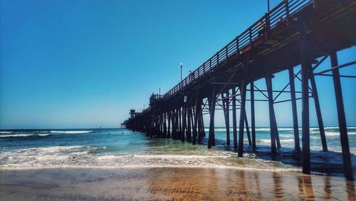 Pier over sea against clear blue sky