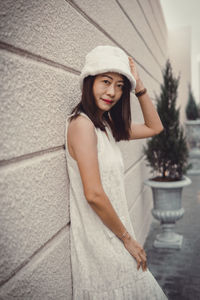 Portrait of young woman standing against wall