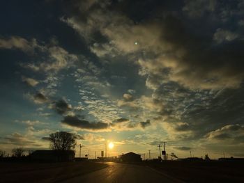 Road by silhouette trees against sky during sunset