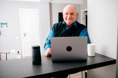 Smiling senior man with laptop sitting at table in home