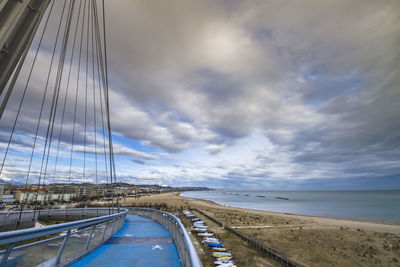 Cropped image of ponte del mare by beach against cloudy sky