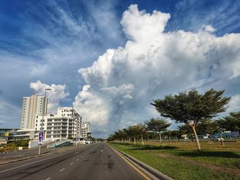 Empty road by buildings in city against sky