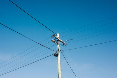 Low angle view of electricity pylon against blue sky