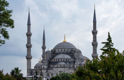 Blue mosque and trees against cloudy sky