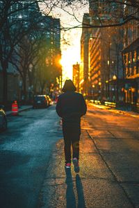 Rear view of man walking on street in city during sunset