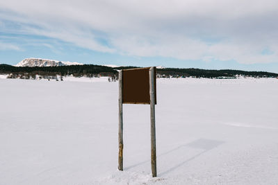 Wooden post on snow covered field against sky