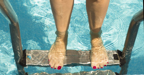 Low section of woman on ladder in swimming pool