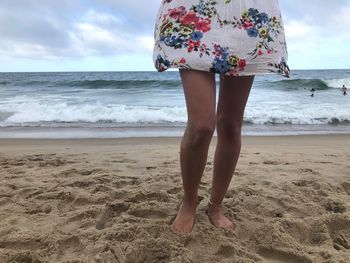 Low section of woman standing at beach against sea