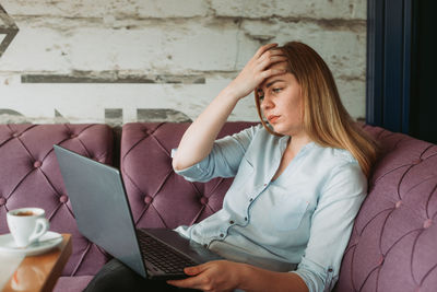 Woman with headache working on laptop, stressful work, bad news via e-mail
