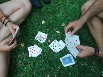 Low section of friends playing cards on grassy field 