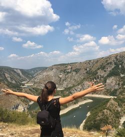 Rear view of woman with arms outstretched standing on mountain against sky