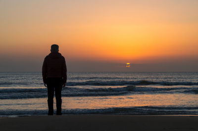 Rear view of silhouette man walking at beach against sky during sunset