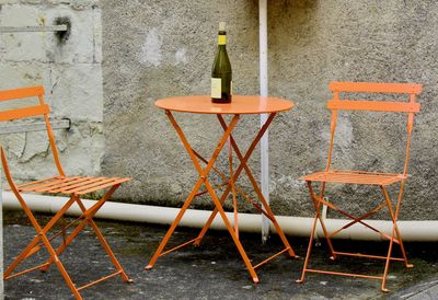 Empty chairs and tables at sidewalk cafe against wall