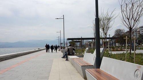 People on footpath by street against sky