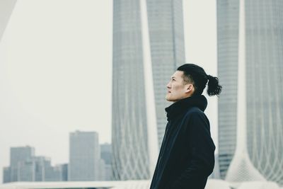 Side view of young woman standing against cityscape