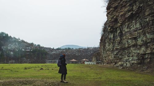 Side view of woman with backpack standing on field against sky