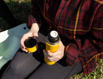 Young woman holds a yellow thermos in her hands, close-up