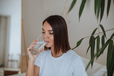Young woman drinking water from a glass at home in the living room