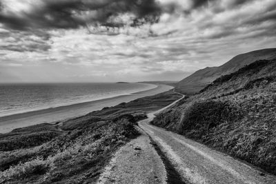 Empty road by beach against cloudy sky