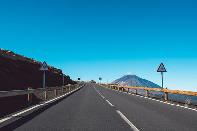 Road leading towards mountain against clear blue sky