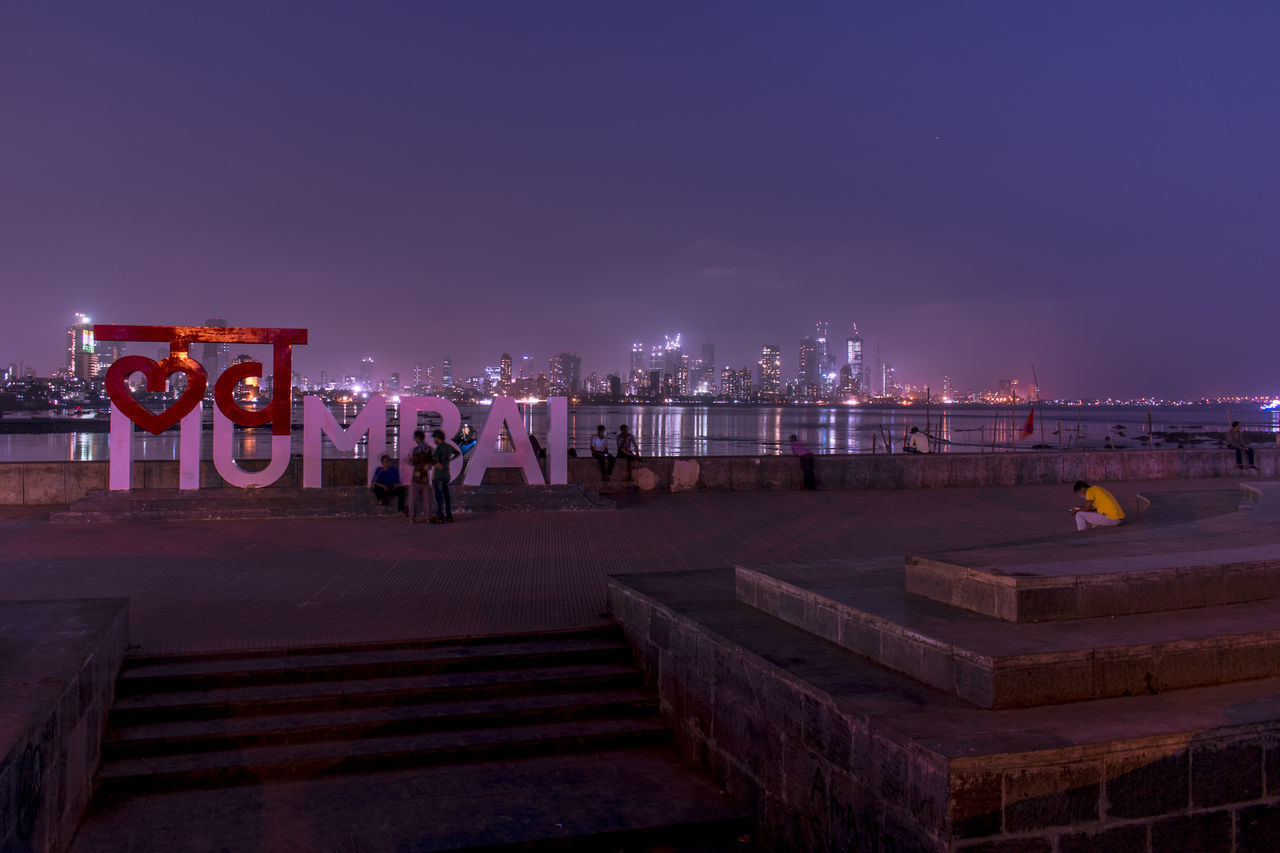 PEOPLE AT ILLUMINATED CITY AGAINST SKY AT NIGHT