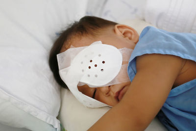 Cute boy with bandage on eye resting on bed