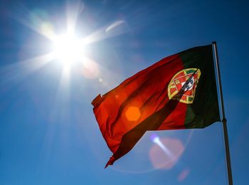 Low angle view of portuguese flag waving against clear blue sky