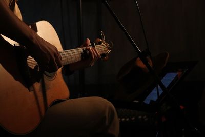 Midsection of musician playing guitar on stage in dark