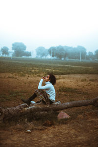 Full length of man sitting on field against sky