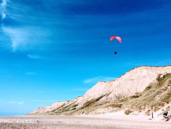 Person paragliding over beach against blue sky